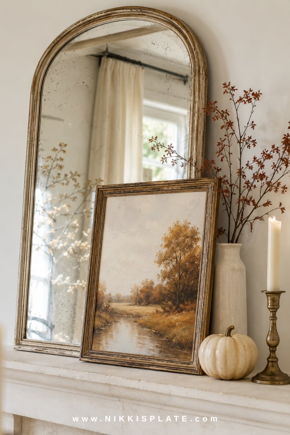 Arched wood mirror anchoring elegant farmhouse fall mantel decor with tall branches, neutral pumpkins and mixed candlesticks.