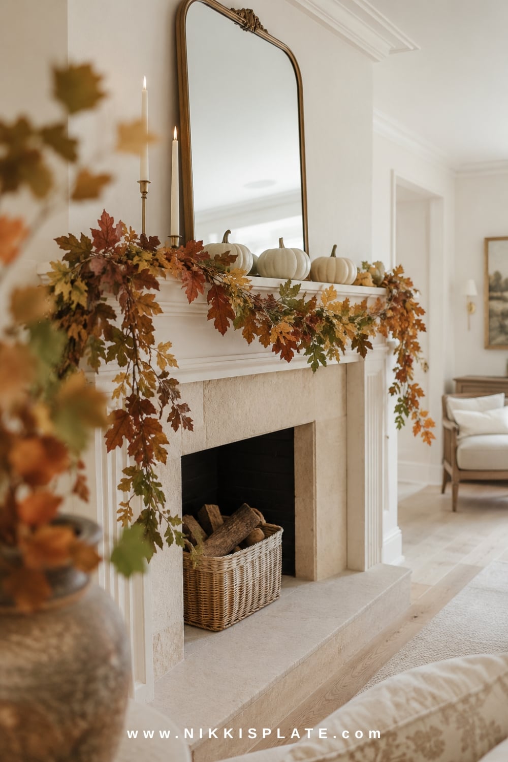 Airy leafy fall mantel garland with oak leaves, eucalyptus, neutral pumpkins and brass candleholders on a white fireplace.