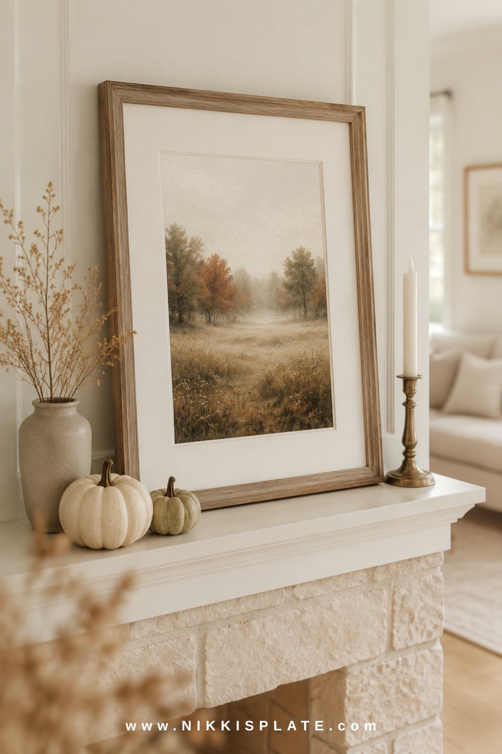 Framed printable fall landscape displayed on a white farmhouse mantel with neutral pumpkins, stoneware and a brass candleholder.