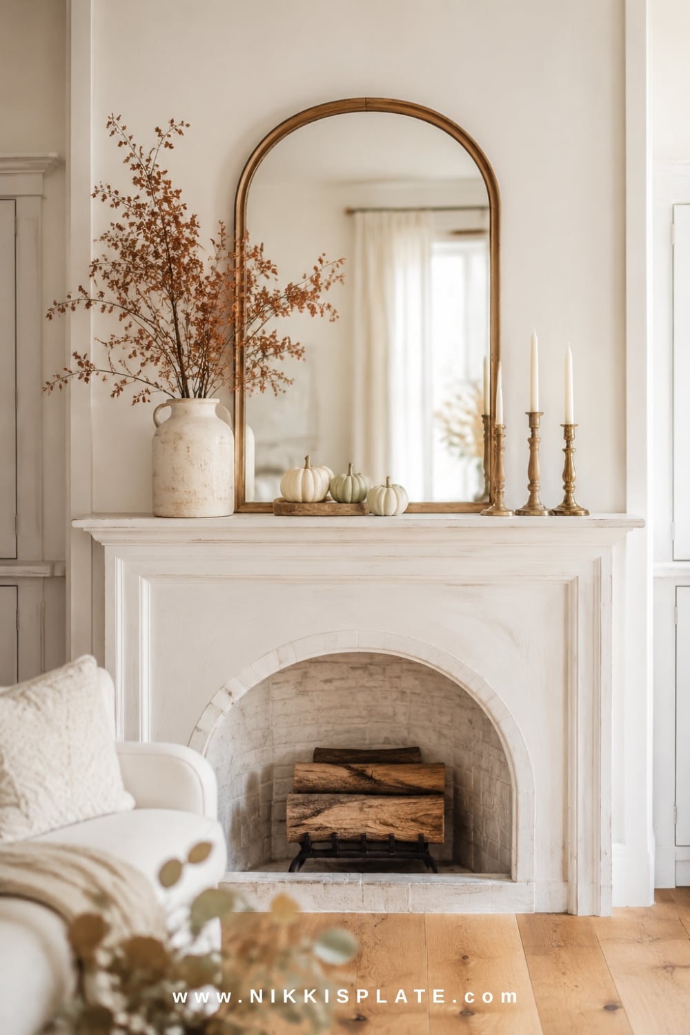 Arched wood mirror anchoring elegant farmhouse fall mantel decor with tall branches, neutral pumpkins and mixed candlesticks.
