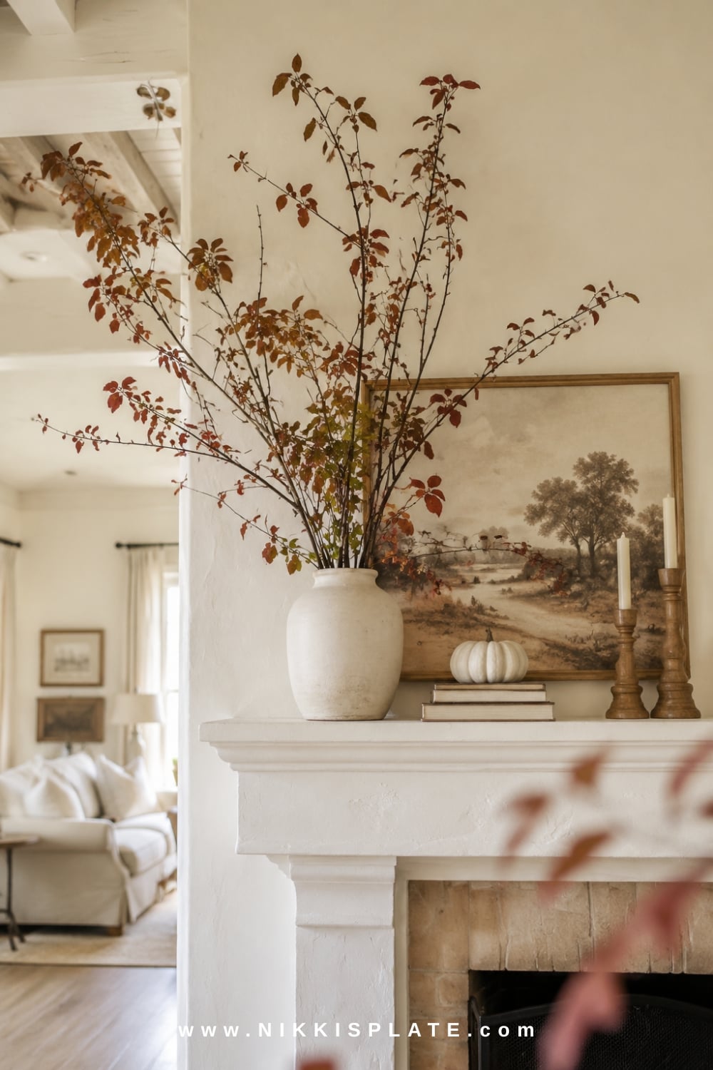 Tall rust and olive fall branches in a cream vase create dramatic height above a bright white fireplace mantel.