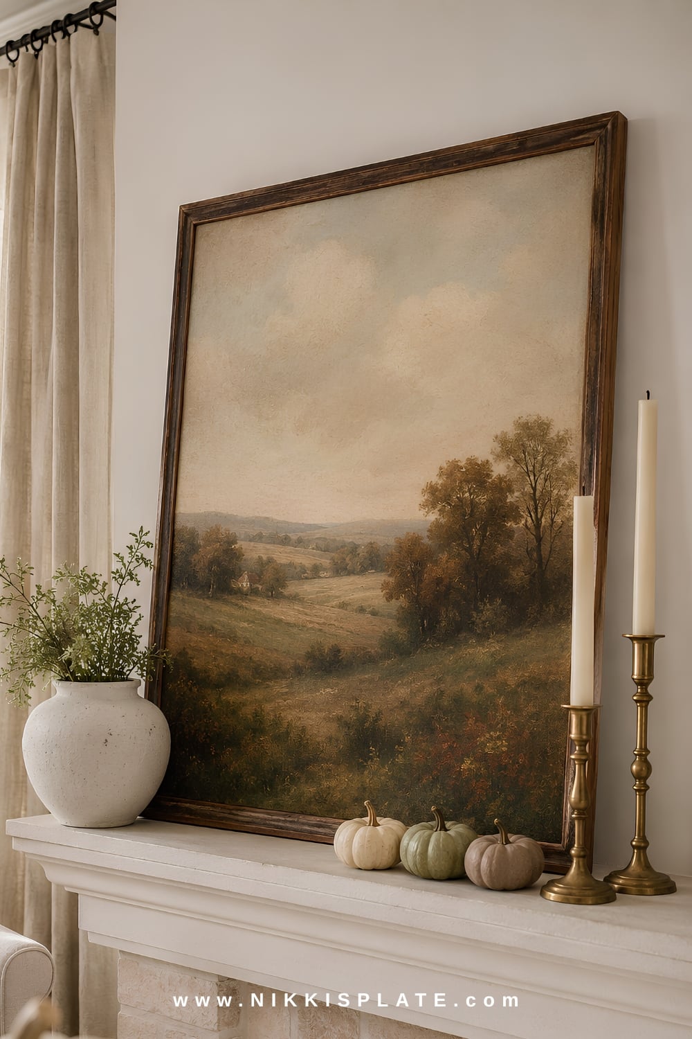 Vintage fall landscape artwork leaned above a warm white mantel styled with cream pottery, brass candlesticks and small pumpkins.