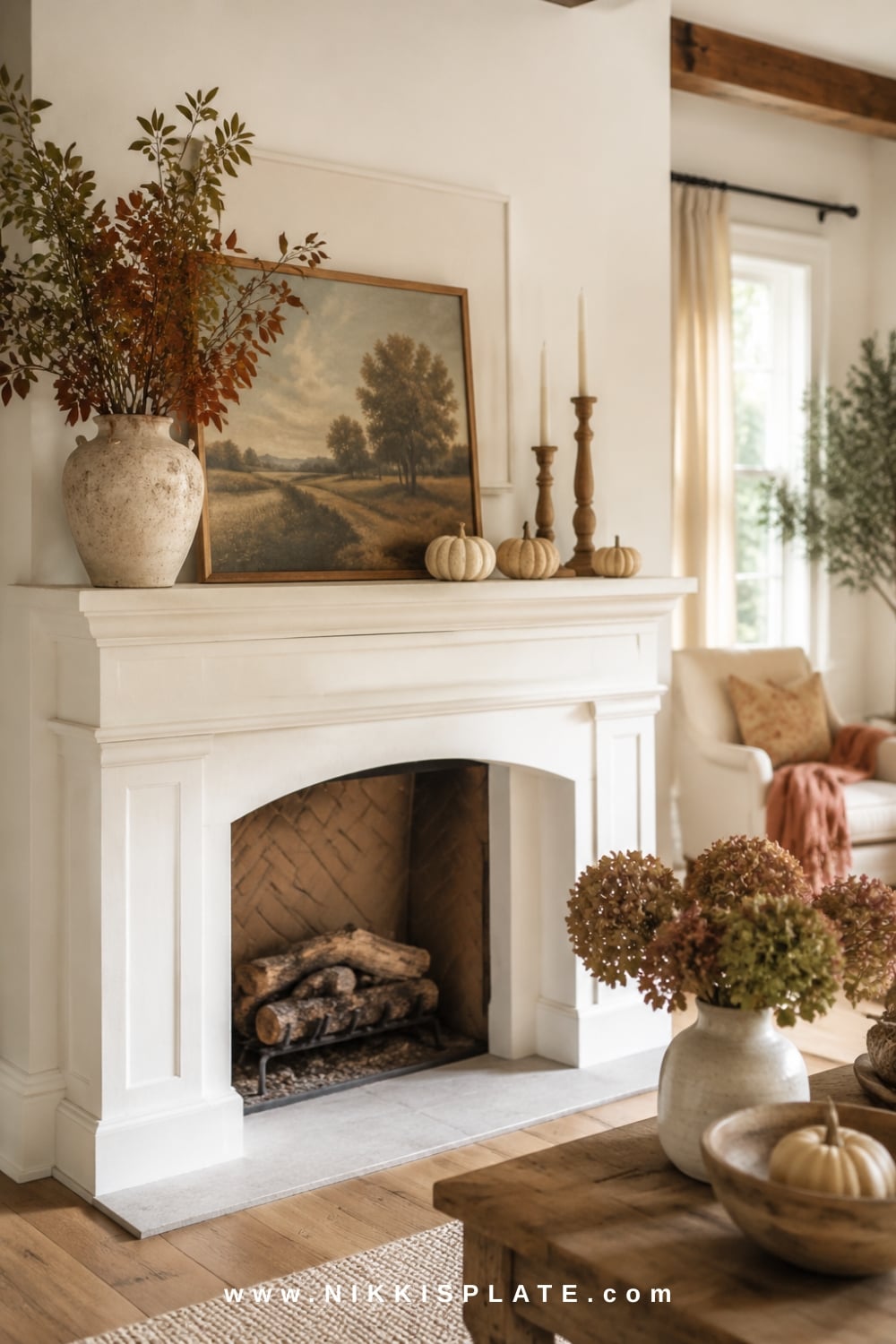 Bright farmhouse fall mantel decor with cream pumpkins, warm wood candlesticks, muted rust leaves and an aged landscape print.