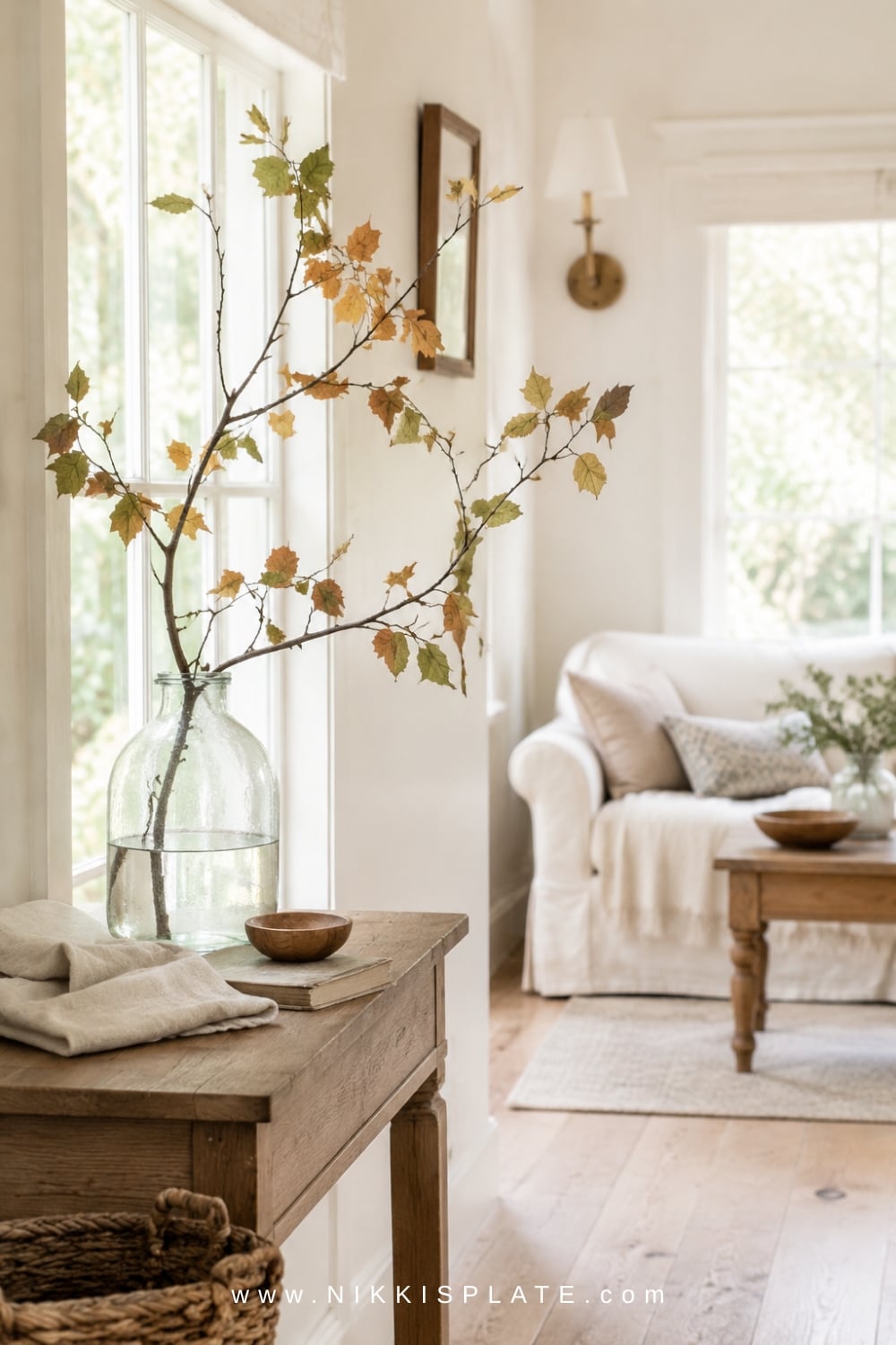 Freshly gathered branches with muted green, gold and rust leaves arranged loosely in a vintage glass vase.