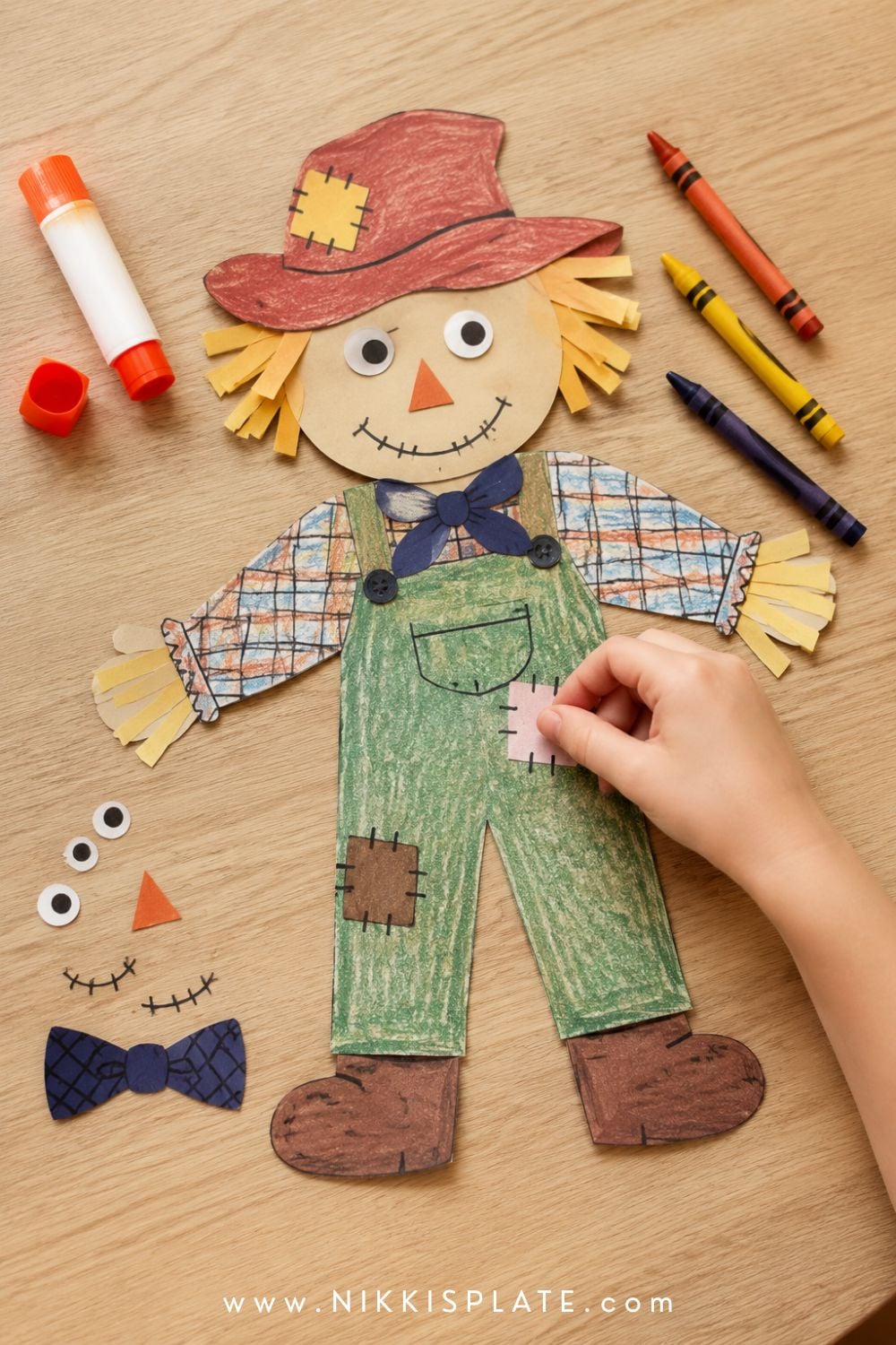 Child gluing a paper patch onto a printable mix-and-match scarecrow with overalls, straw hair and a floppy hat.