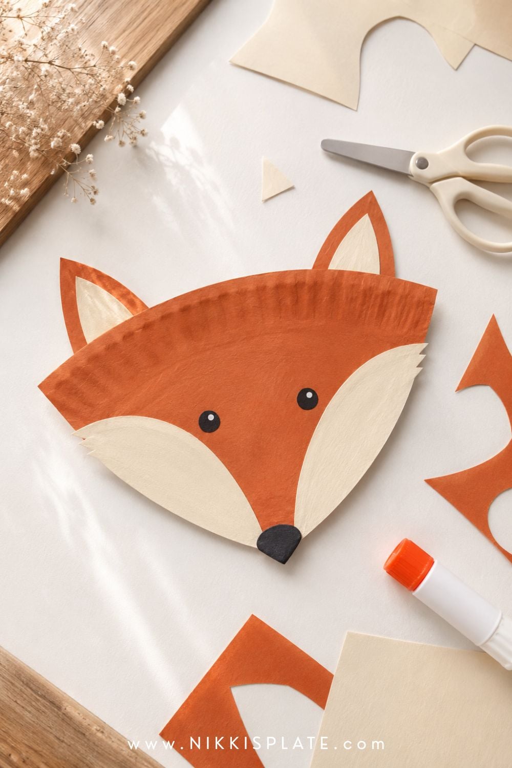 Paper plate fox fall craft for kids with an orange face, cream cheeks, pointed ears and a black nose.