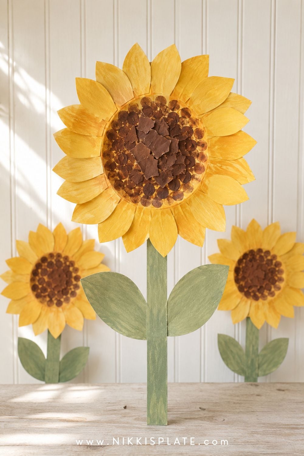 Paper plate sunflower craft for kids with golden petals, a textured brown center and green paper leaves.