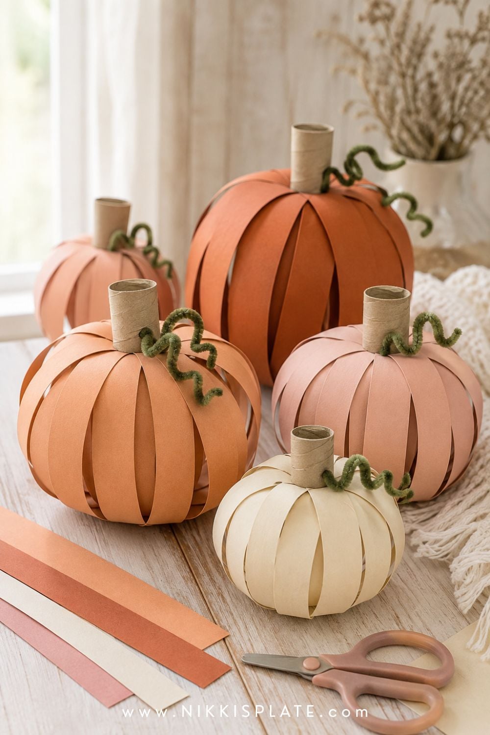 Three-dimensional paper strip pumpkins in orange, cream and blush with stems and curled green vines.