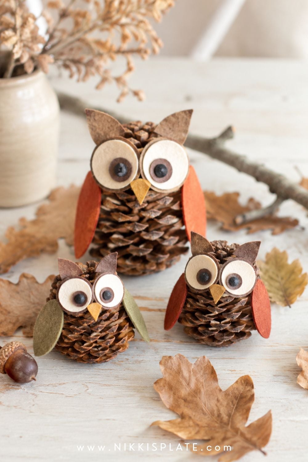Pinecone owl craft family with layered paper eyes, tiny beaks and rust-colored wings in a woodland setting.