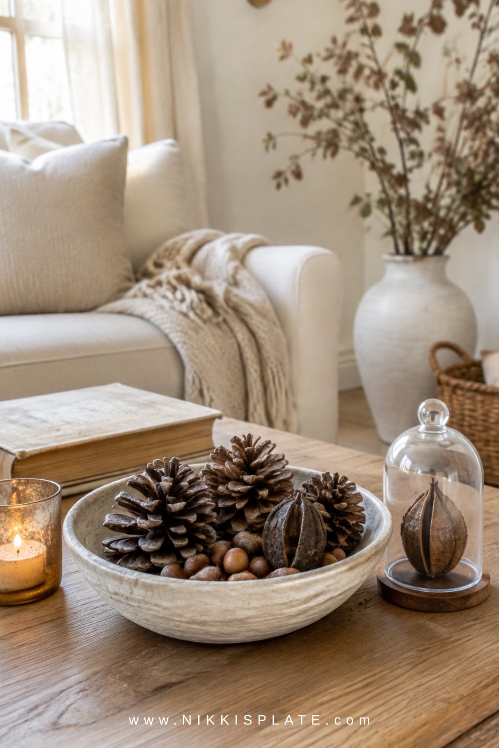 Cream pottery bowl holding pinecones, acorns and seed pods as simple natural fall coffee table decor.