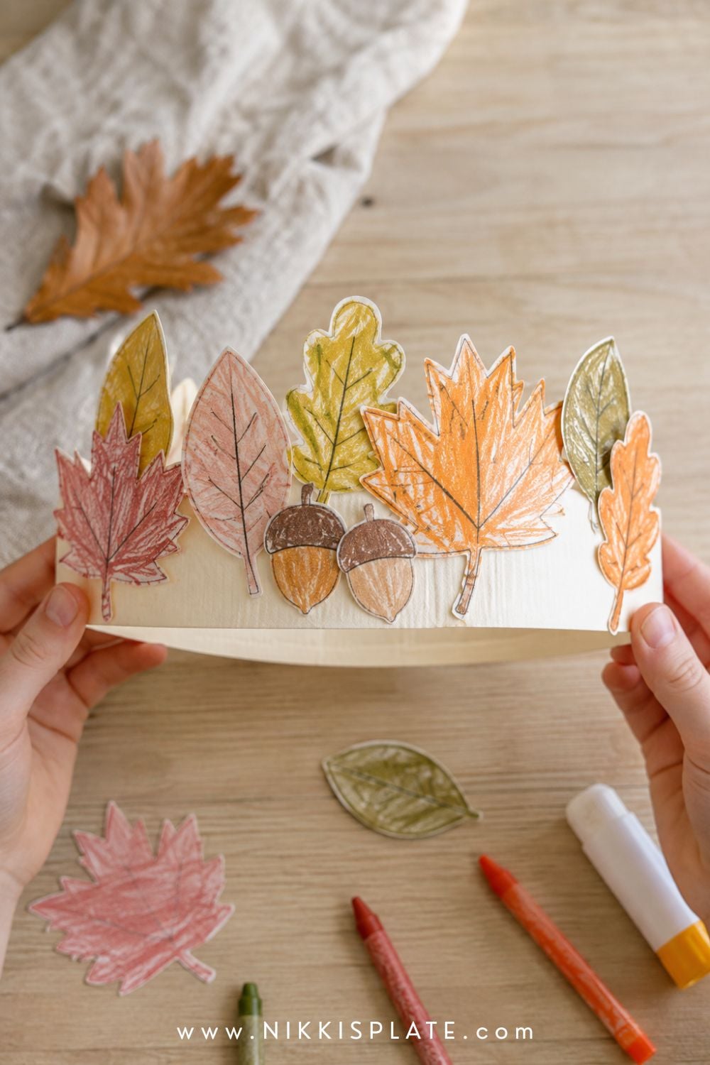 Child holding a printable fall leaf crown decorated with hand-coloured maple leaves, oak leaves and paper acorns.