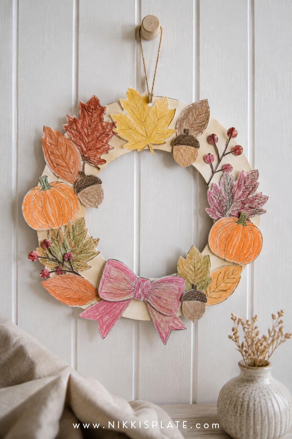 Child-made printable fall wreath decorated with paper leaves, pumpkins, acorns, berries and a simple bow.