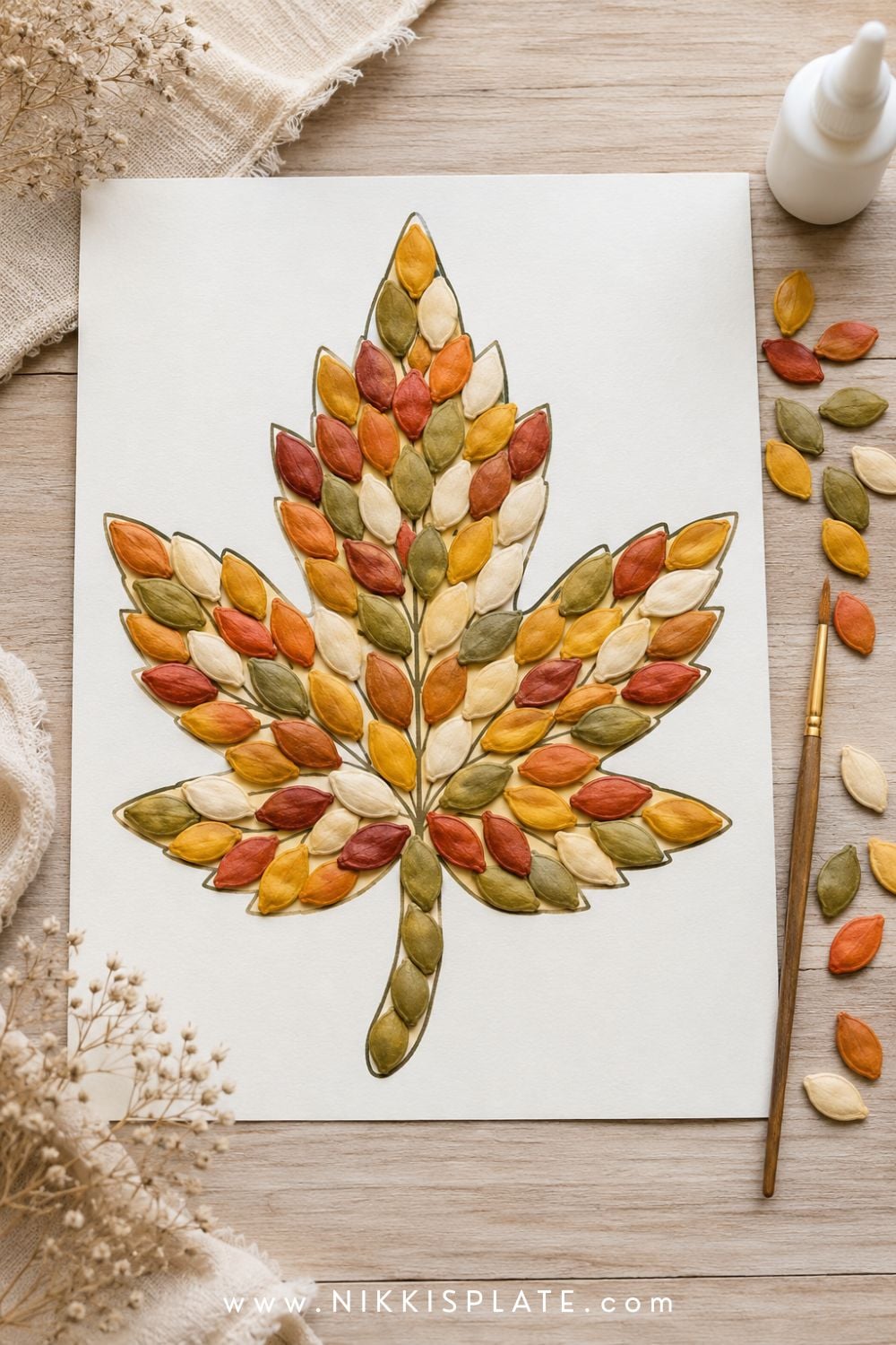 Pumpkin seed mosaic fall craft featuring a leaf shape filled with painted seeds in muted autumn colors.
