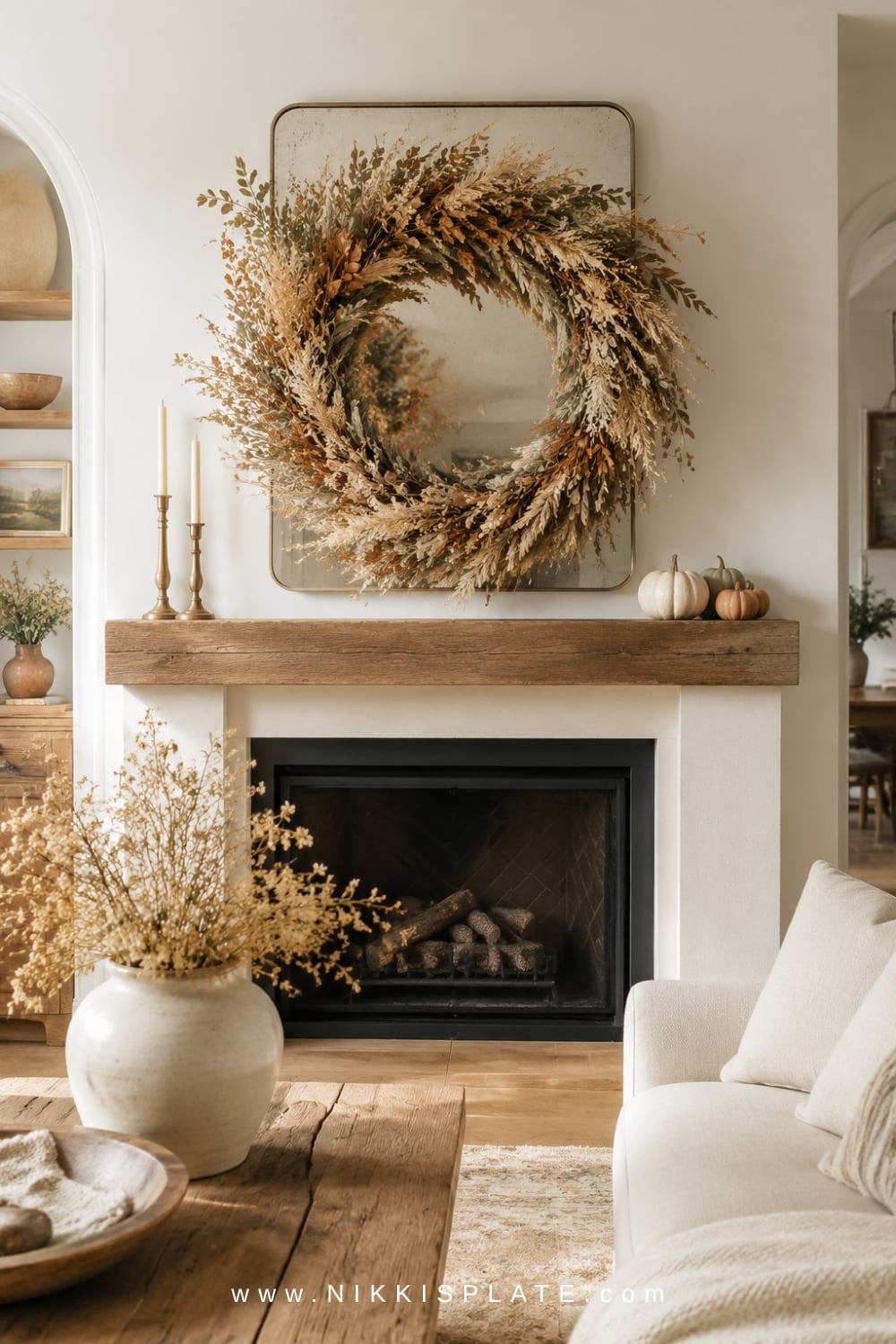 Oversized neutral fall wreath of dried leaves, wheat and greenery displayed above a white fireplace.