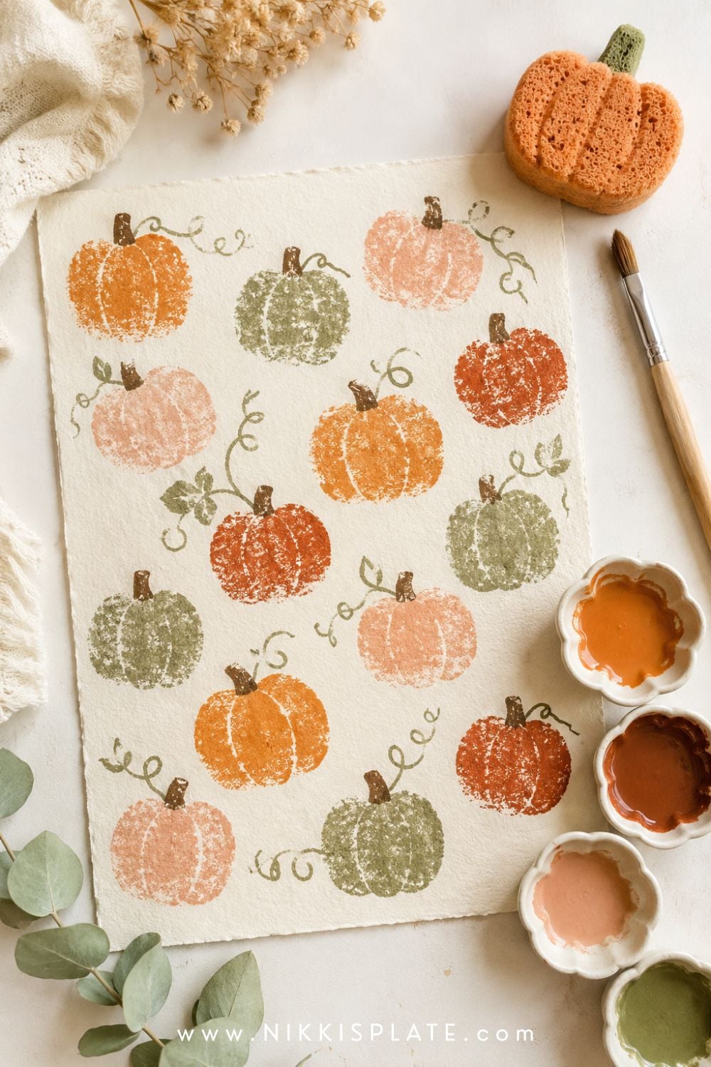 Sponge-painted pumpkin craft for kids with orange, rust and green pumpkin stamps across cream paper.