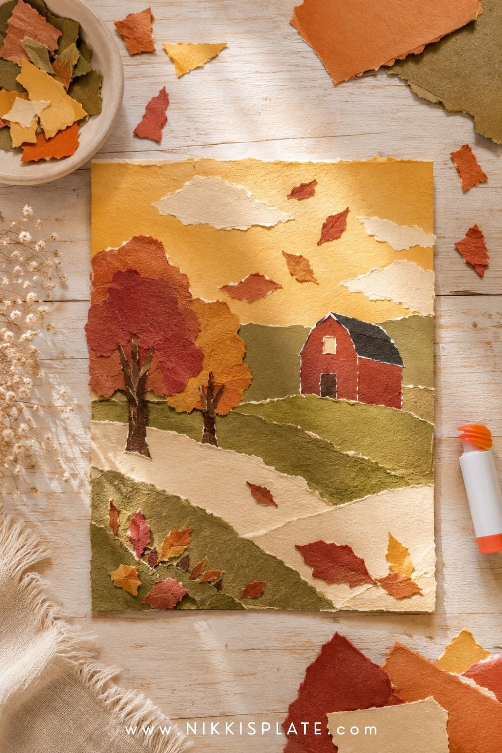 Torn paper autumn landscape with rolling fields, colorful trees, a red barn and scattered fall leaves.