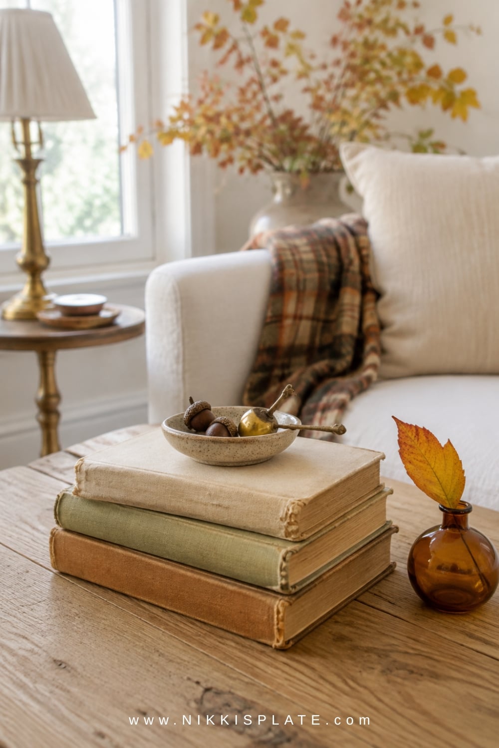 Stacked vintage books with warm neutral covers styled beside a ceramic vase and brass accent on a fall coffee table.