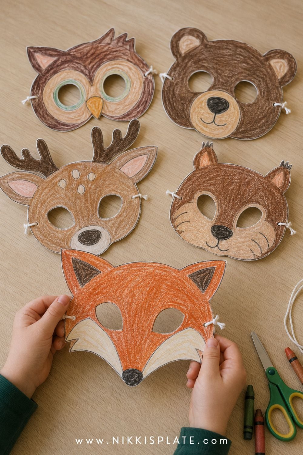 Five child-coloured woodland animal masks featuring a fox, owl, bear, deer and squirrel on a craft table.
