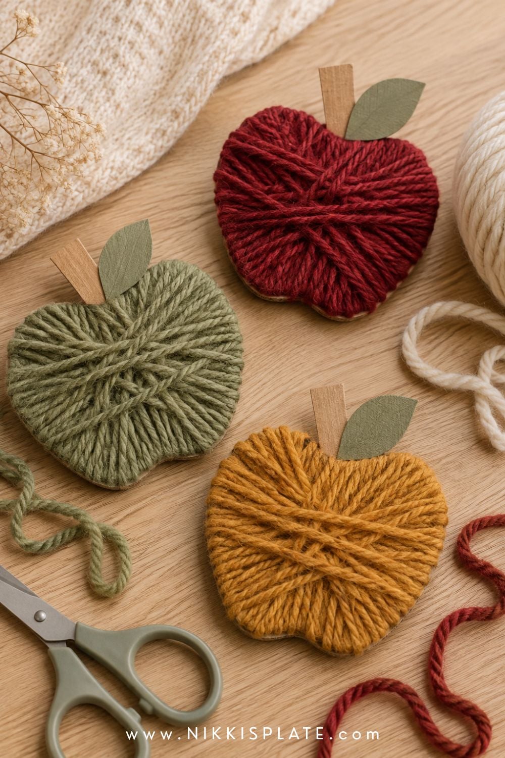 Yarn-wrapped cardboard apples in red, green and mustard for a cozy, low-mess fall craft for kids.