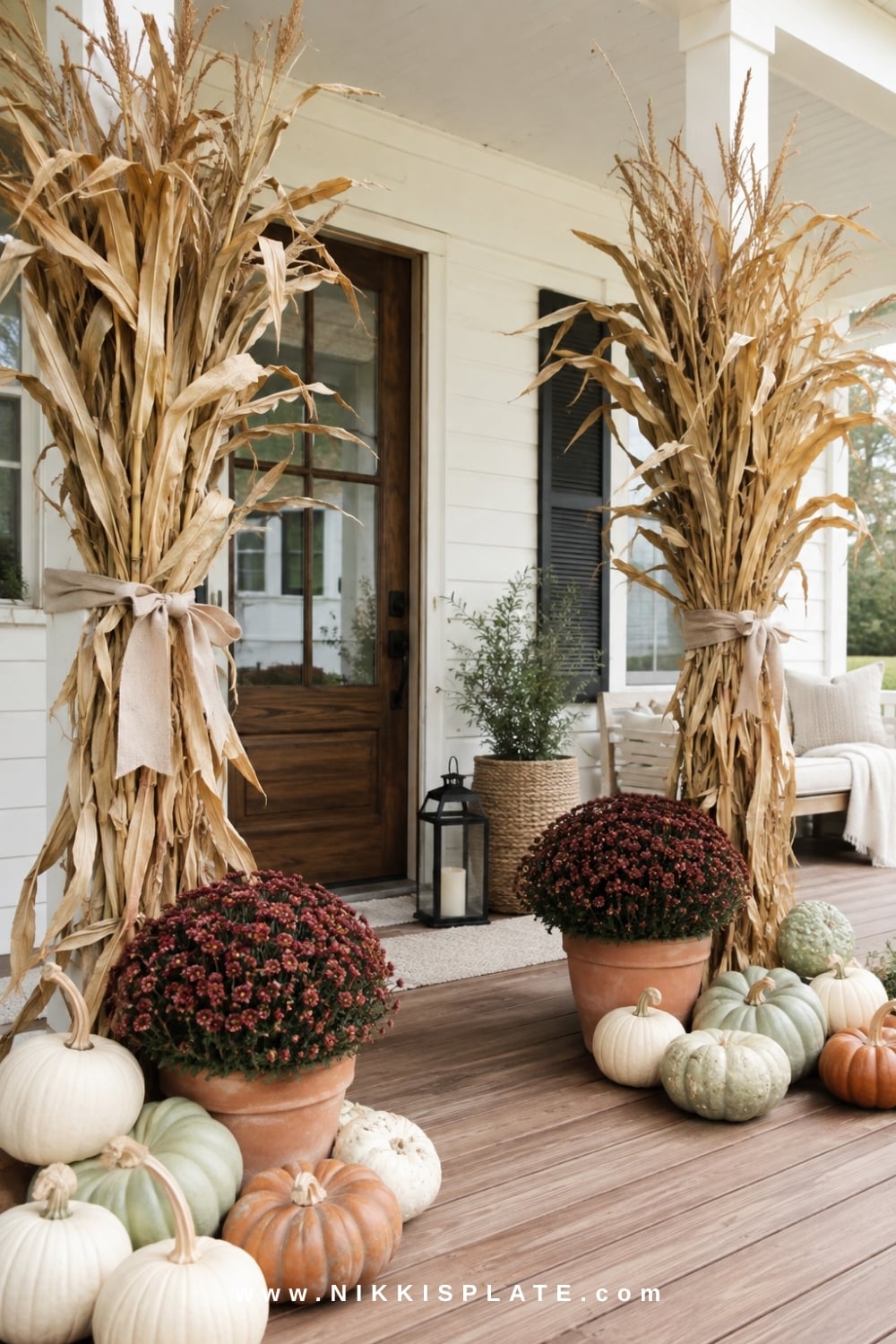 Farmhouse entrance framed with cornstalk bundles, heirloom pumpkins, burgundy mums and a black lantern.