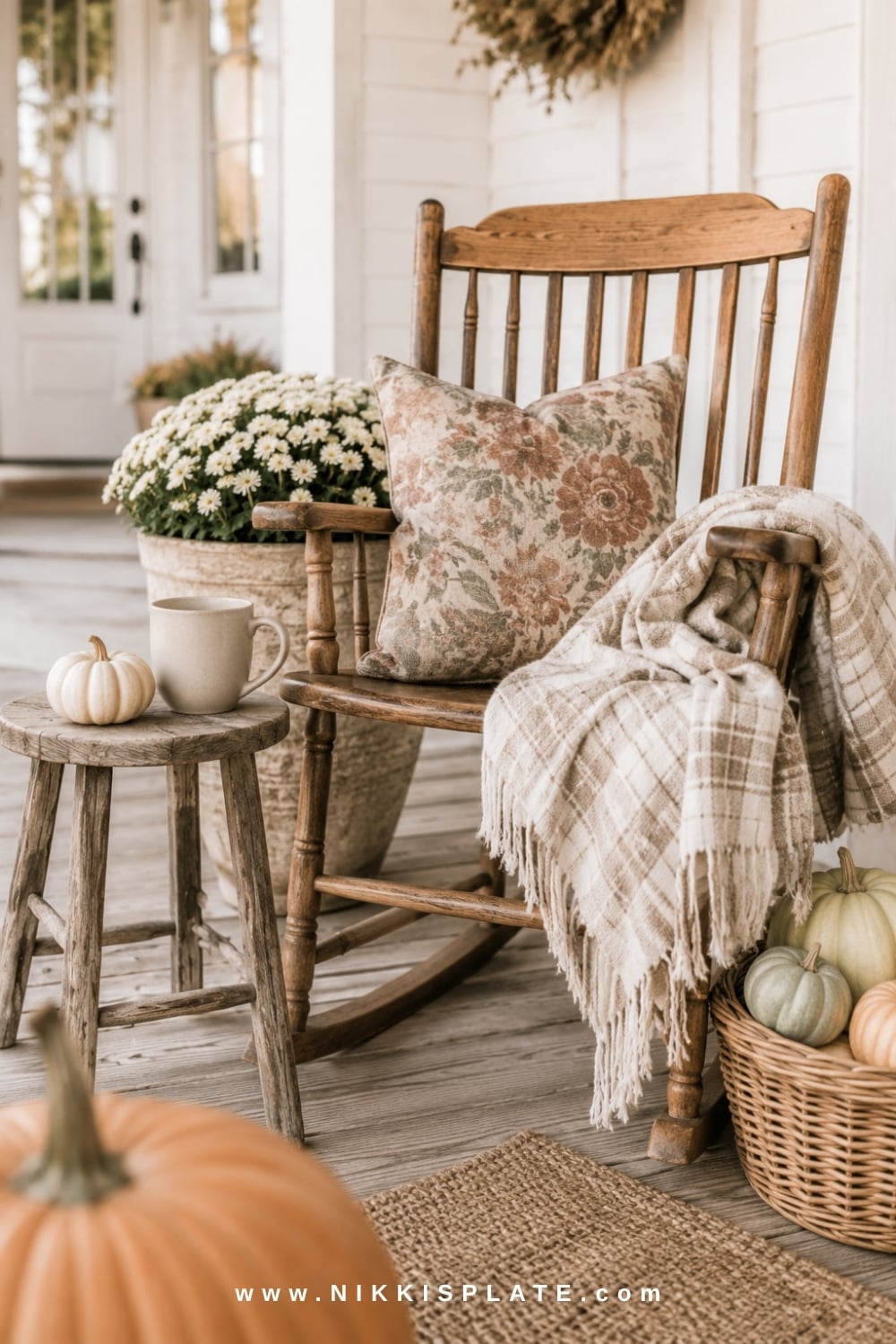 Wooden porch chair styled with a plaid blanket, floral pillow, pumpkins and cream fall mums.