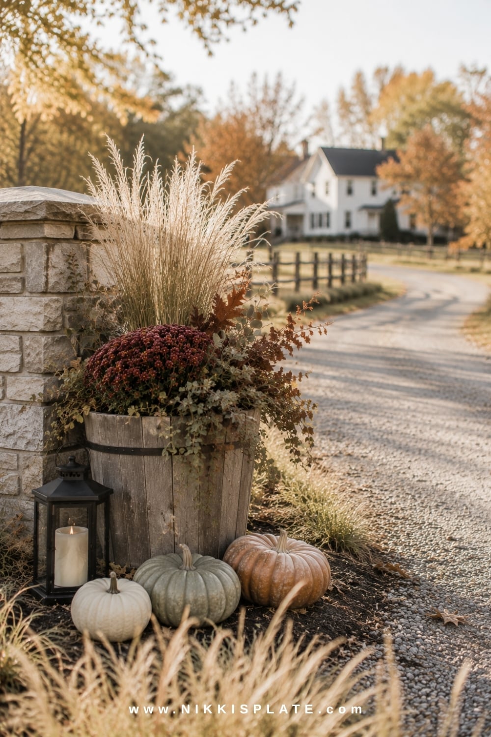 Farmhouse driveway entrance decorated with a wood planter, ornamental grasses, mums and pale pumpkins.