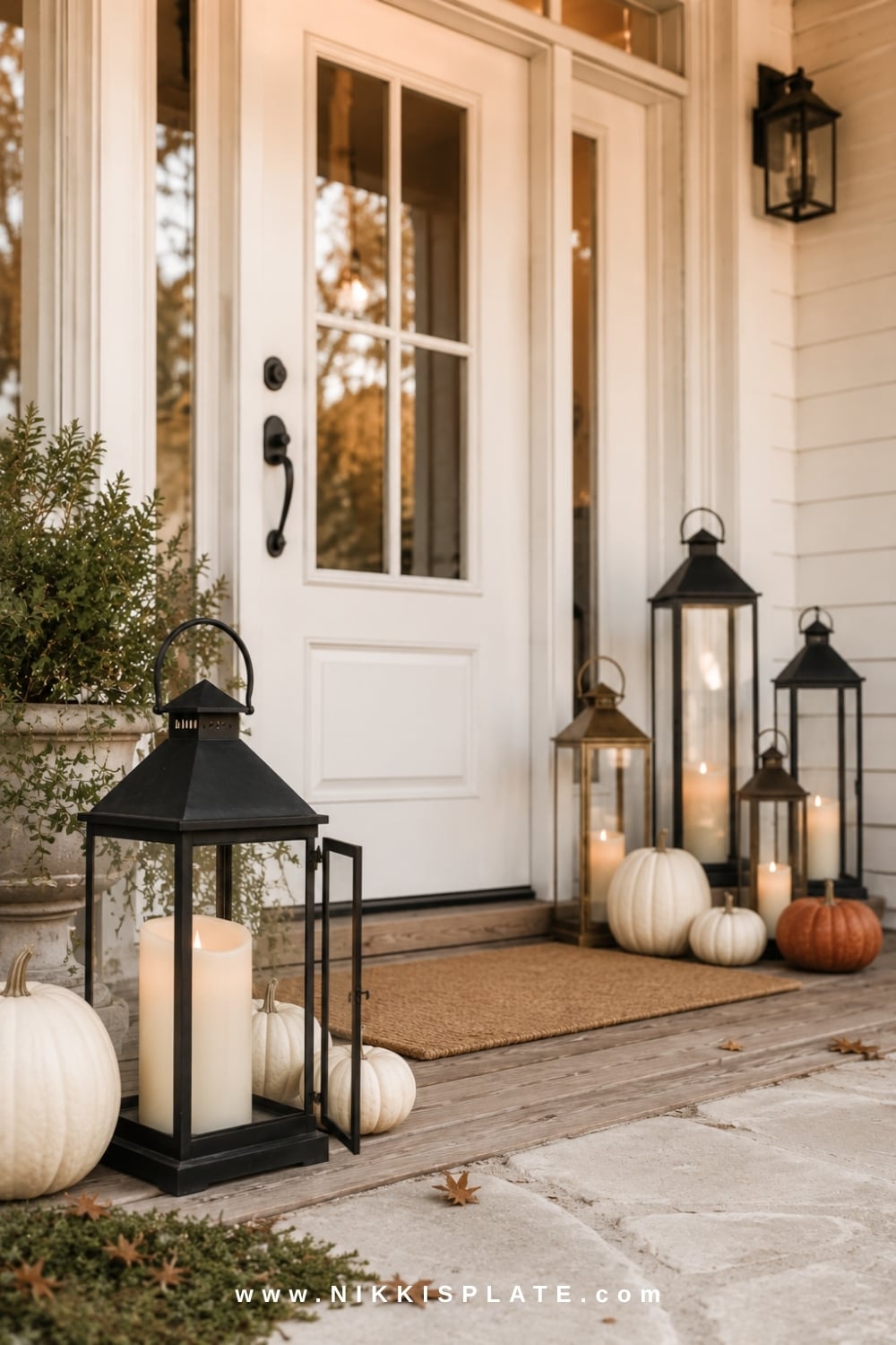 Black and aged brass lanterns with flameless candles arranged around a white farmhouse front door.