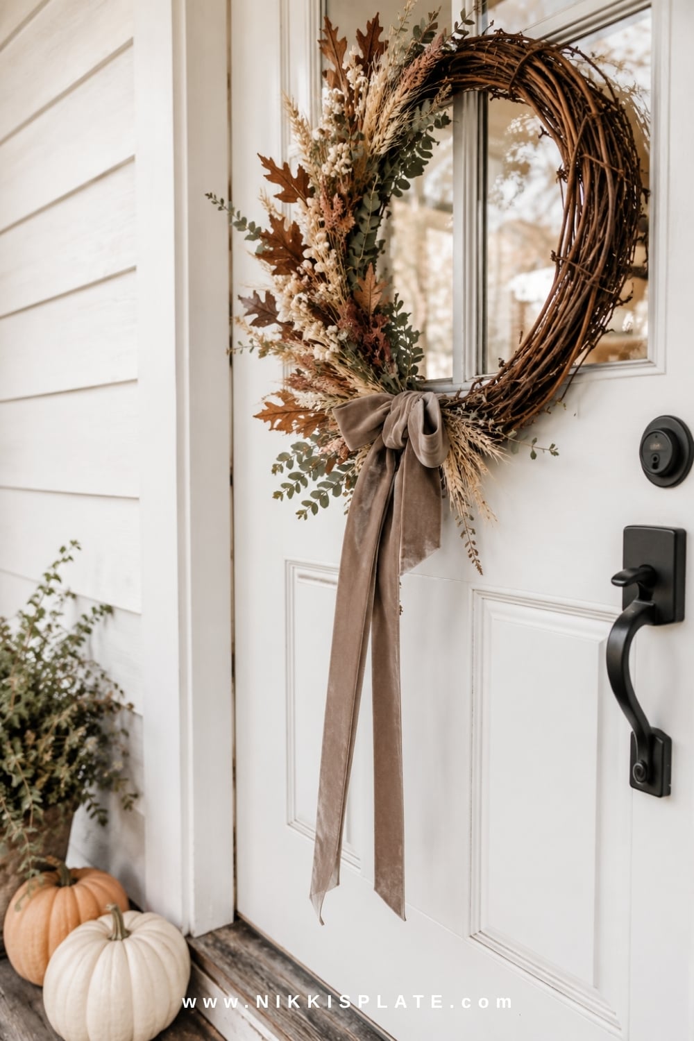 Grapevine fall wreath with rust leaves, dried wheat and velvet ribbon on a white farmhouse front door.