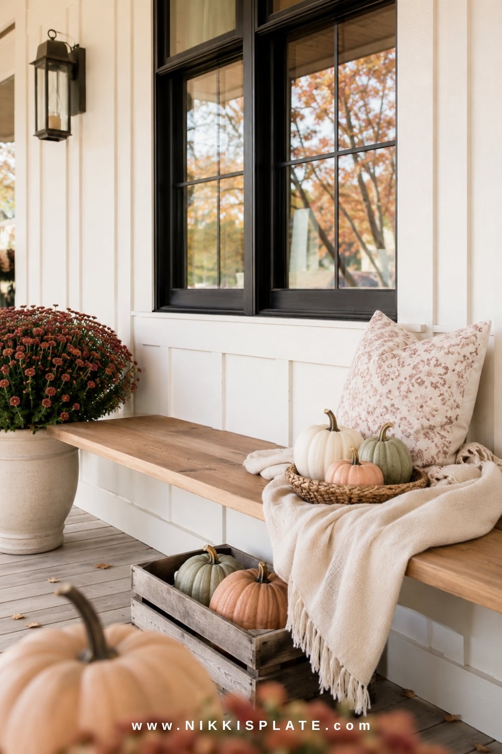 Farmhouse porch bench decorated with a soft throw, fall pillow, woven pumpkin basket and burgundy mums.