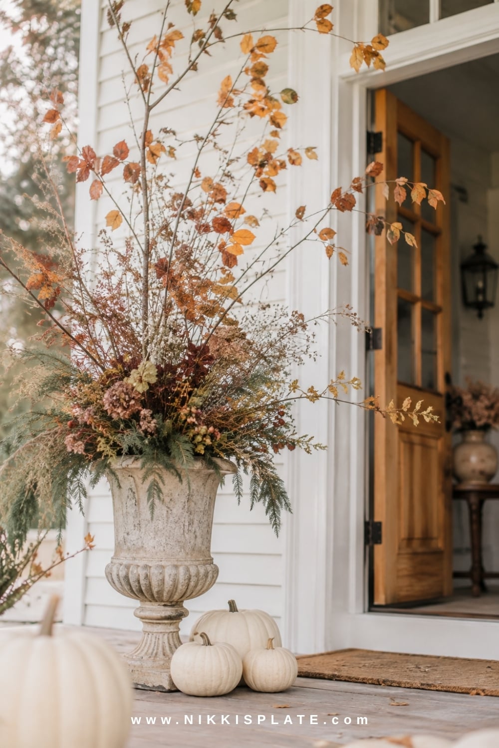 Tall stone urn filled with foraged autumn branches, dried grasses, rose hips and evergreen clippings.