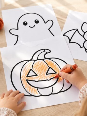 Toddler coloring a smiling pumpkin beside simple Halloween coloring pages with bold outlines and large open spaces.