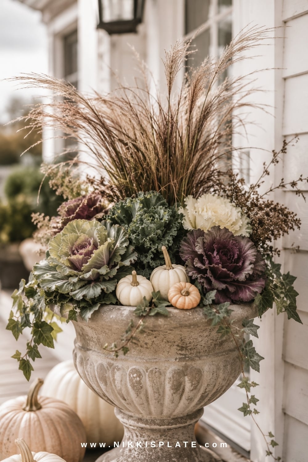 Stone fall planter filled with ornamental cabbage, bronze grasses, ivy and miniature pumpkins.