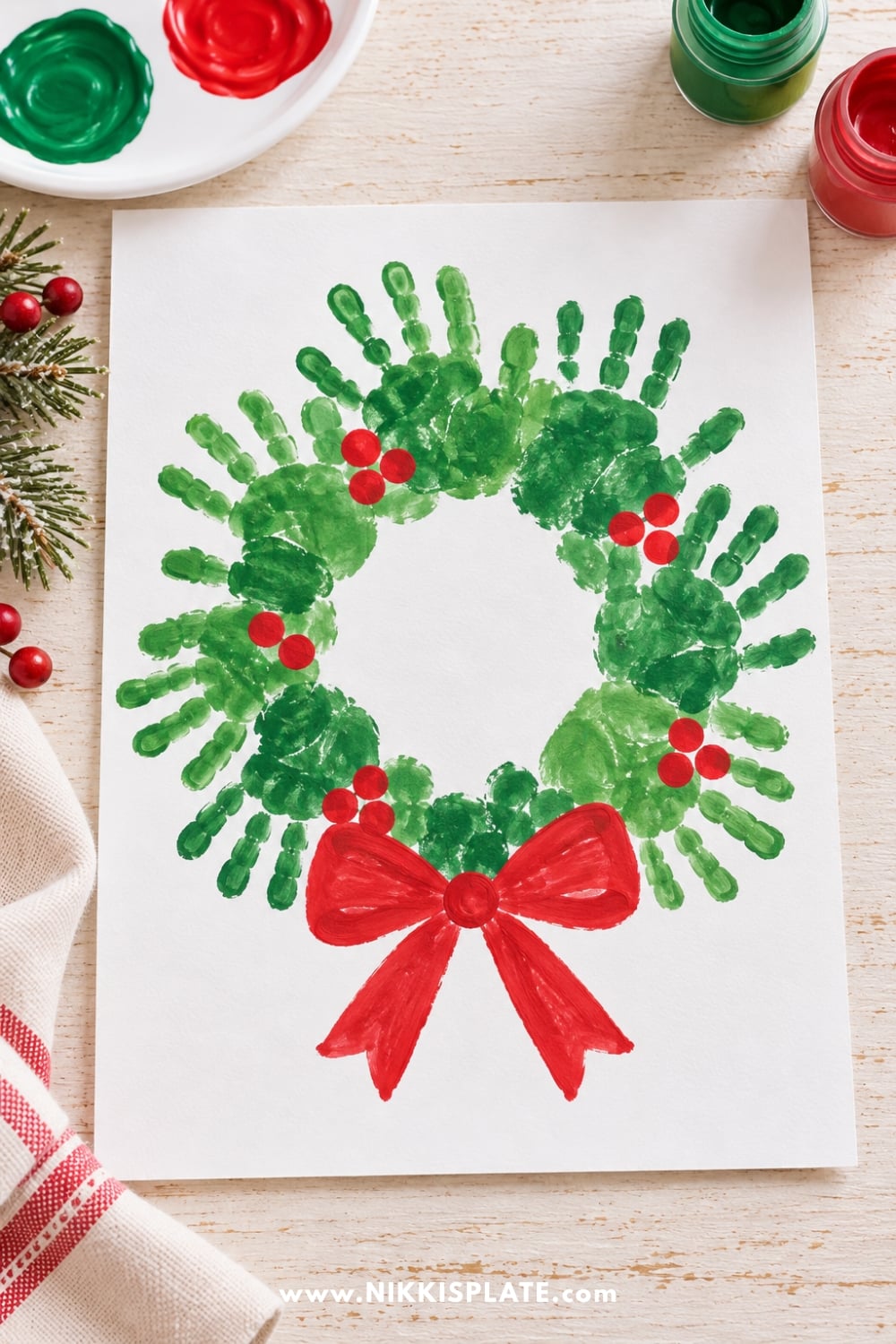 Christmas handprint wreath made with overlapping green handprints, red fingerprint berries, and a painted red bow.